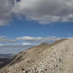 A rocky slope extends upward toward a ridgeline under a blue sky with scattered clouds.