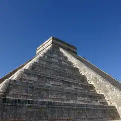 A pyramid with multiple tiers and a flat top, constructed from stone blocks, set against a clear blue sky.