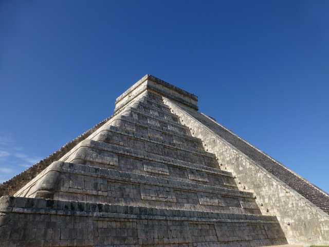 A pyramid with multiple tiers and a flat top, constructed from stone blocks, set against a clear blue sky.