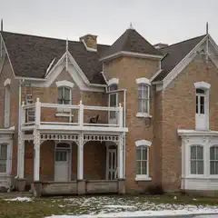 A two-story brick house with white trim and a dark brown roof. It is set amidst partially snowy lawns.