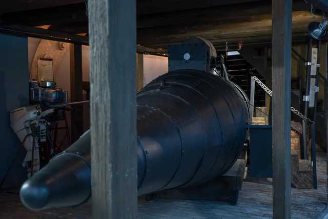 A dark gray submarine occupies the center of a room with wooden support beams and walls.