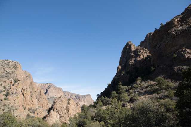 A rugged mountain pass with steep cliffs and sparse vegetation under a clear blue sky.