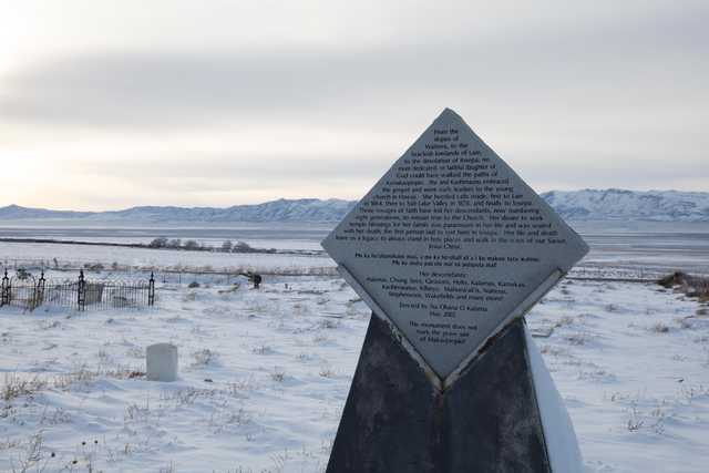 A diamond-shaped monument stands in a snowy cemetery with mountains in the background.