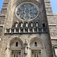 A stone church facade features a large rose window, ornate carvings, and double doors with decorative ironwork.