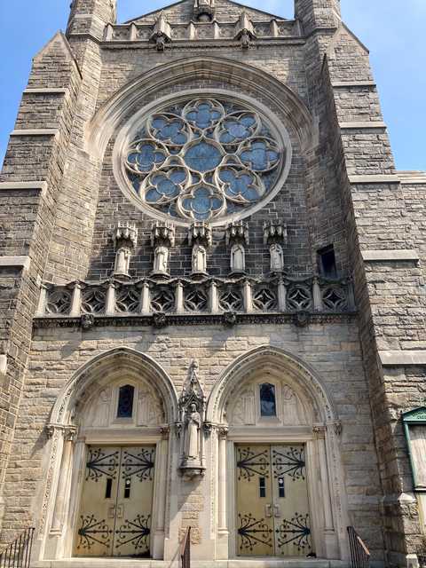 A stone church facade features a large rose window, ornate carvings, and double doors with decorative ironwork.