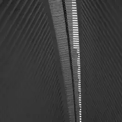 A narrow, slatted skylight runs between two steeply angled, ribbed walls, creating a strong geometric contrast in black and white.