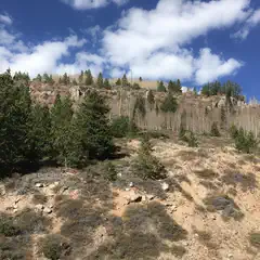 A rocky hillside covered with sparse trees and shrubs under a partly cloudy sky.
