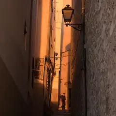 A narrow alleyway between buildings with a staircase leading up to an entrance. A person appears at the top of the stairs.