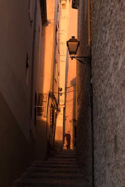 A narrow alleyway between buildings with a staircase leading up to an entrance. A person appears at the top of the stairs.