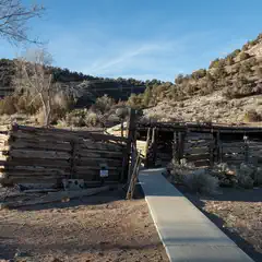 A concrete pathway leads to a dilapidated wooden structure in a desert landscape.