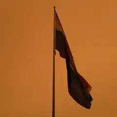 A rainbow pride flag flying on a flagpole, set against an orange-tinted sky.