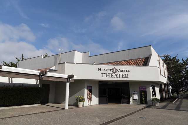 Hearst Castle Theater is a single-story building with a tiled gable roof, modernist design, and textured concrete exterior.