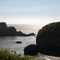 A coastal landscape features rocky islands and a calm sea under a clear sky.