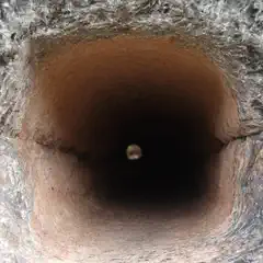 A circular opening in a textured stone surface leads into a dark, hollow interior.