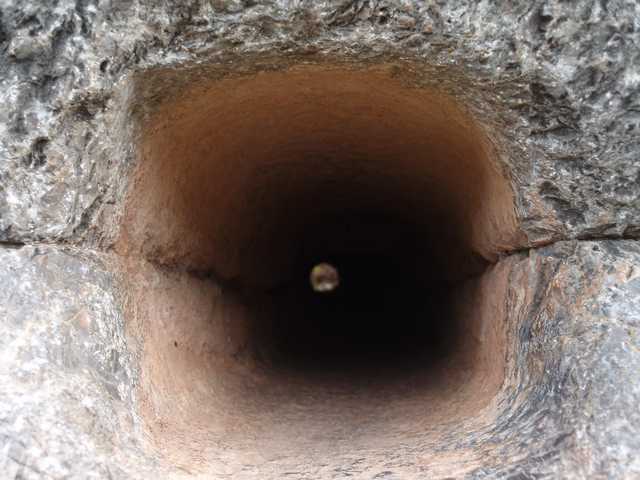 A circular opening in a textured stone surface leads into a dark, hollow interior.