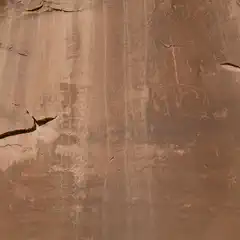 A tan rock face displays petroglyphs of human-like figures, animals, and geometric shapes.