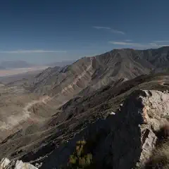 A rocky outcrop overlooking a vast desert landscape with distant mountains under a clear blue sky.