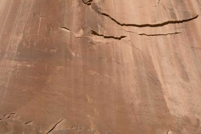 A textured sandstone wall features faint petroglyphs and natural erosion patterns.