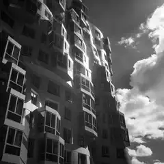 A high-rise residential building features staggered, curved balconies and reflective surfaces under a partly cloudy sky.