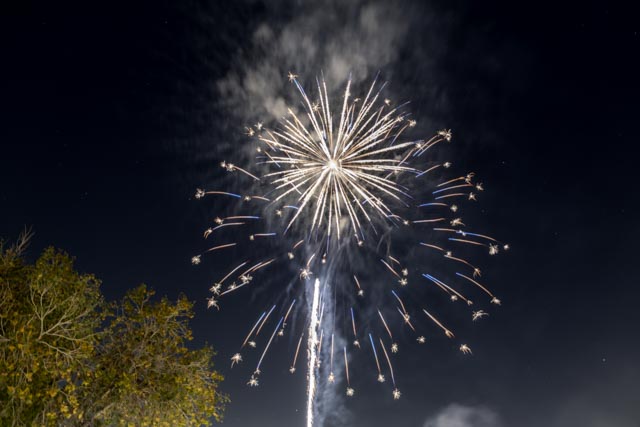 A large fireworks explosion fills the dark sky with white and gold trails.