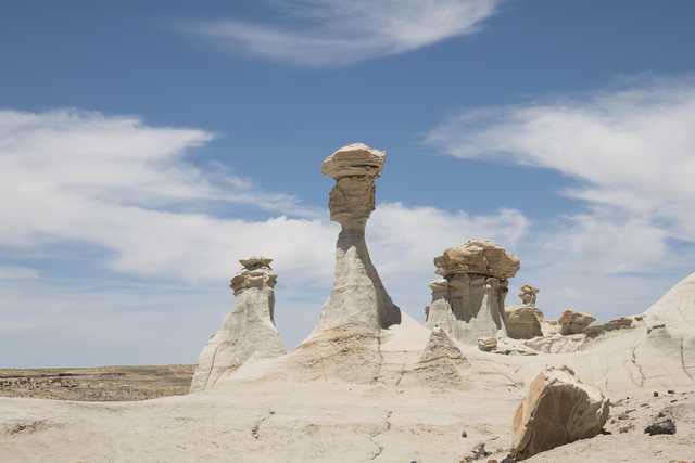 Eroded rock formations stand tall against a clear blue sky in a barren desert landscape.