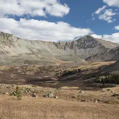 A valley filled with dry grasses sits between three steep, rocky mountains under a blue sky with scattered clouds.
