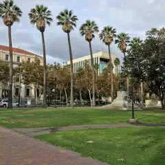 A paved walkway leads to a grassy area with tall palm trees and a statue on a pedestal.