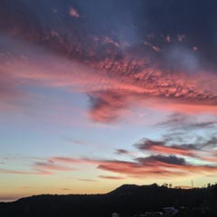A vibrant sunset sky transitions from deep blue to fiery reds and pinks, with scattered clouds reflecting the light, above a silhouetted hillside.