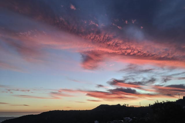 A vibrant sunset sky transitions from deep blue to fiery reds and pinks, with scattered clouds reflecting the light, above a silhouetted hillside.