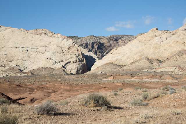 A canyon cuts through tan rock formations under a clear blue sky.