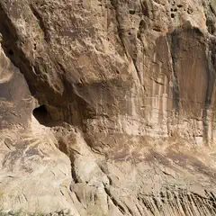 A rugged cliff face with layered rock formations and a small cave-like opening.