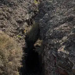 A rugged volcanic landscape features a deep fissure cutting through rocky terrain, with sparse vegetation clinging to the edges.
