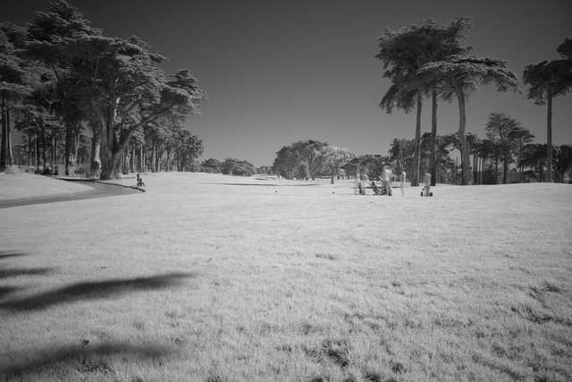 A golf course with a large open field and trees lining the horizon under a clear sky.