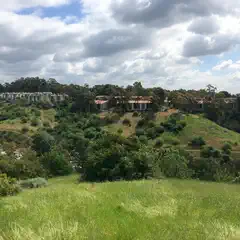 A hilly landscape with a cluster of houses on top and lush greenery below under a partly cloudy sky.