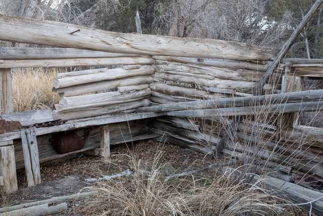 A partially collapsed log structure sits among dry grasses and brush.