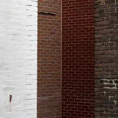 A vertical composition of four distinct brick walls, ranging from white to dark brown, with varied textures and mortar lines.