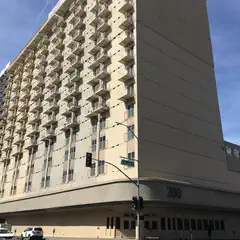 A tall beige hotel building with numerous balconies and windows occupies the corner of a city street intersection.