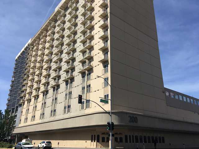 A tall beige hotel building with numerous balconies and windows occupies the corner of a city street intersection.