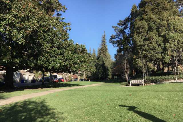 A paved path runs through a grassy area with several trees and a bench.