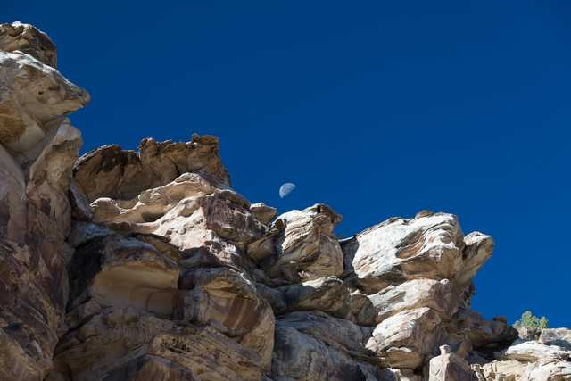 A rocky cliff face under a clear blue sky with the moon visible above it.