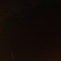 A streaking meteor trails across a star-filled night sky.