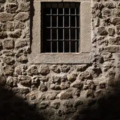 A barred window on a stone wall, with sunlight casting shadows and highlighting textures.