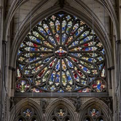 A large, intricate rose window with colorful stained glass is set within a pointed Gothic arch, flanked by stone columns and tracery.
