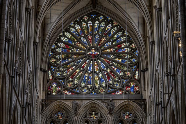 A large, intricate rose window with colorful stained glass is set within a pointed Gothic arch, flanked by stone columns and tracery.