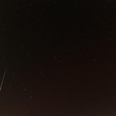 A meteor streaks across a star-filled night sky.