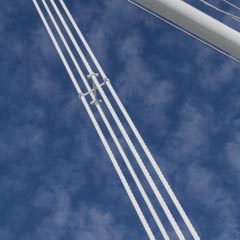 White cables and a structural beam of a bridge extend diagonally against a blue sky with scattered clouds.