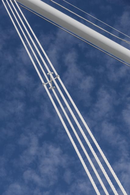 White cables and a structural beam of a bridge extend diagonally against a blue sky with scattered clouds.