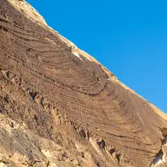 A rock formation with ridges from erosion or weathering, set against a blue sky.