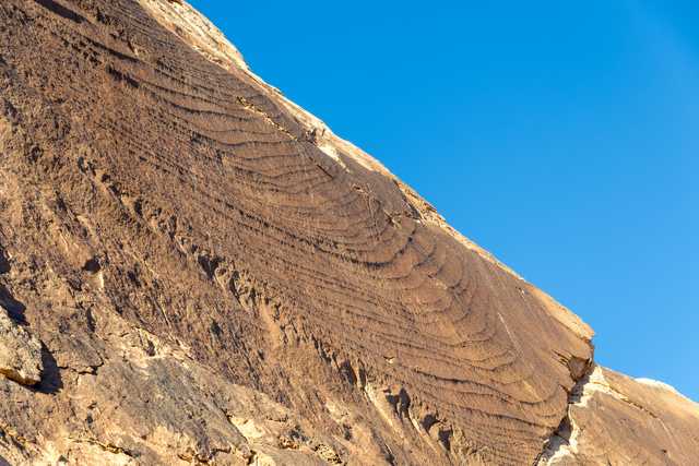 A rock formation with ridges from erosion or weathering, set against a blue sky.