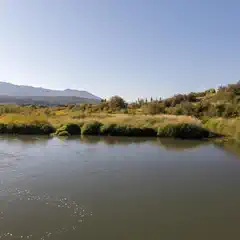 A calm river flows through a lush, green landscape with distant mountains under a clear blue sky.